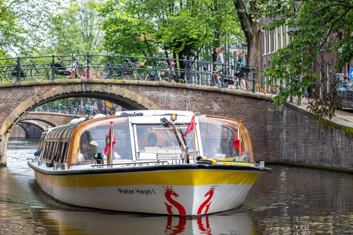 A canal cruise boat passes under a bridge in Amsterdam