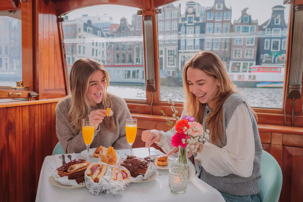Two women enjoy brunch and drinks during a daytime Amsterdam canal cruise.