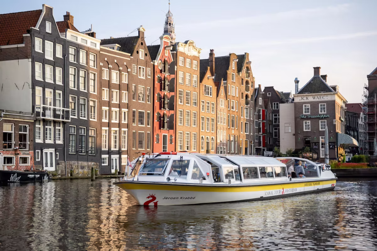 A canal tour boat passes by historic Amsterdam canal houses on the waterfront.