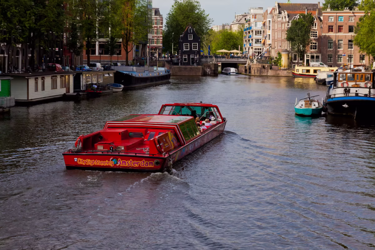 A red sightseeing boat cruises through an Amsterdam canal.