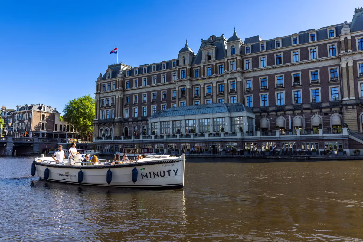 A private canal boat cruises past a luxury hotel on the Amsterdam waterfront.