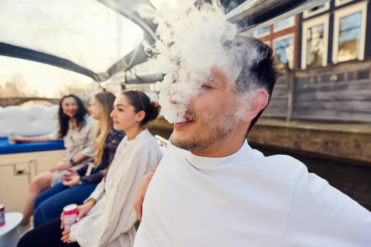 Friends relax on an Amsterdam canal cruise while one person blows smoke.