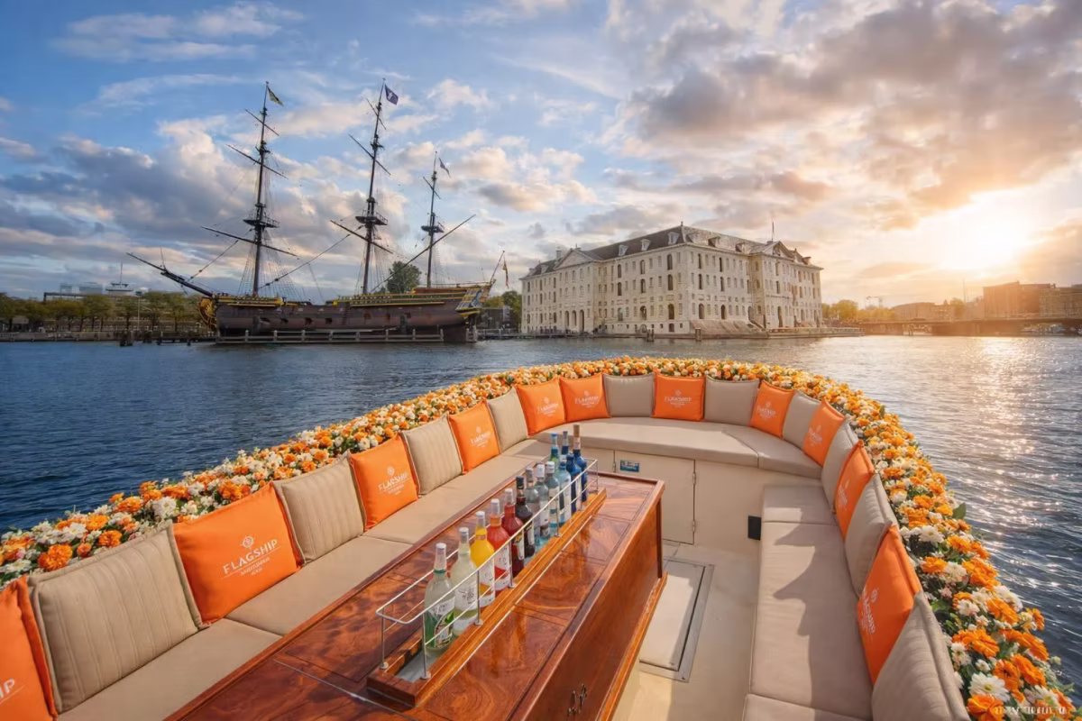 A glass-roof canal cruise boat travels through Amsterdam on a clear day.