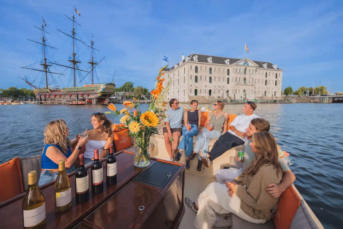 Guests enjoy drinks on an Amsterdam canal cruise near the Maritime Museum and a historic sailing ship.
